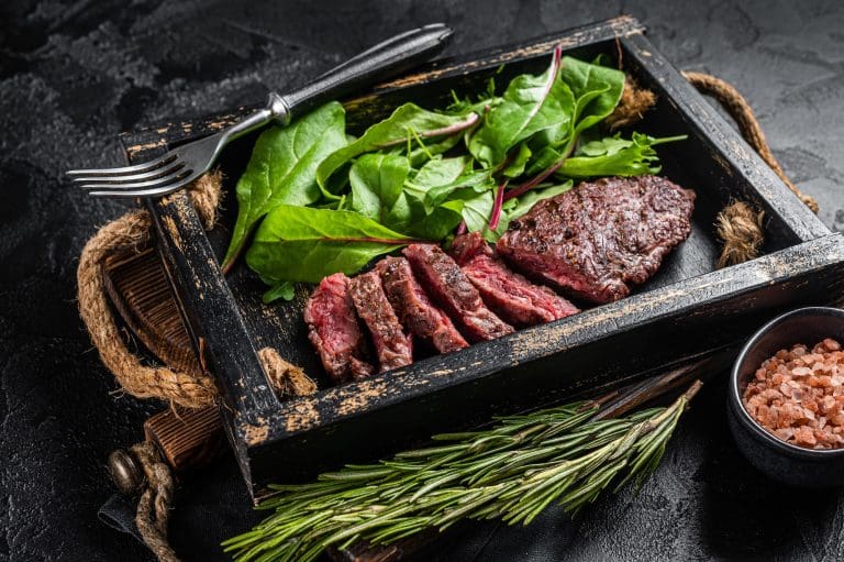 BBQ roasted flank steak in wooden tray with vegetable salad. Black background. Top view