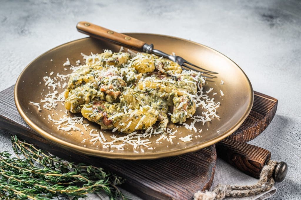 Cooked Gnocchi potato pasta with spinach and parma ham on plate. White background. Top view
