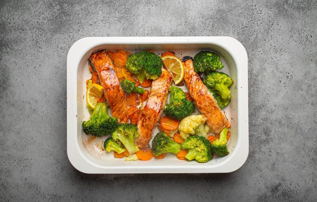 Top view of healthy baked fish salmon steaks, broccoli, cauliflower, carrot in casserole dish