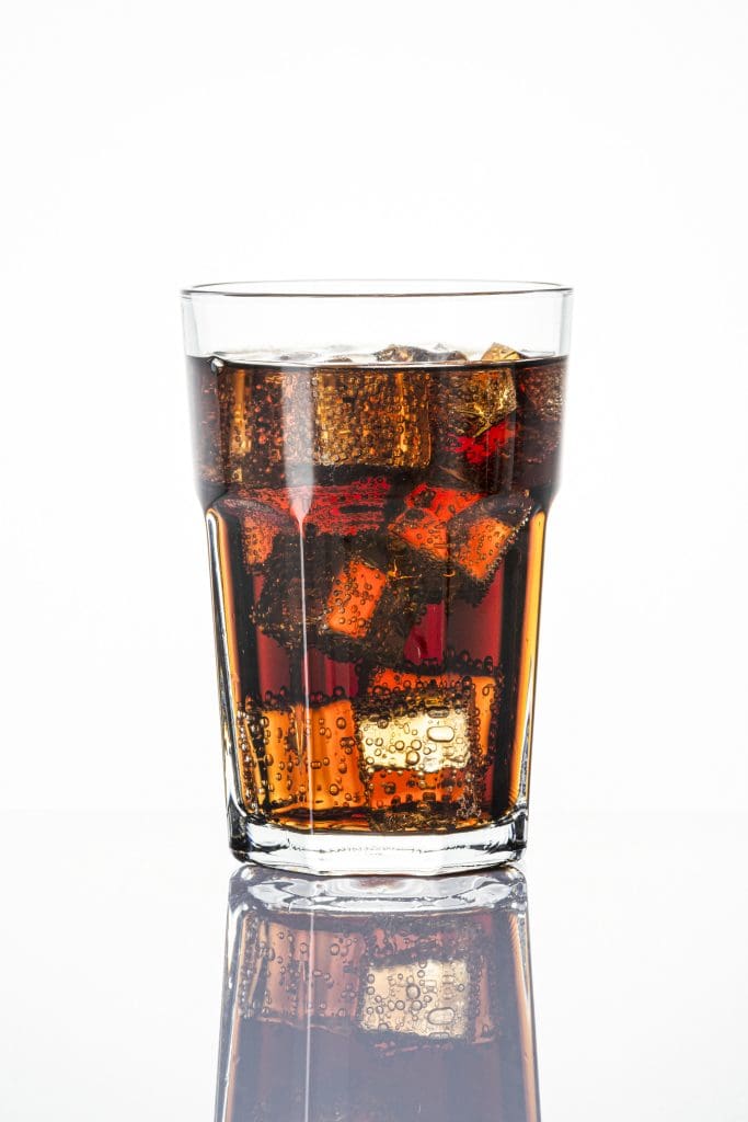 Cold carbonated drink over ice cubes in a glass