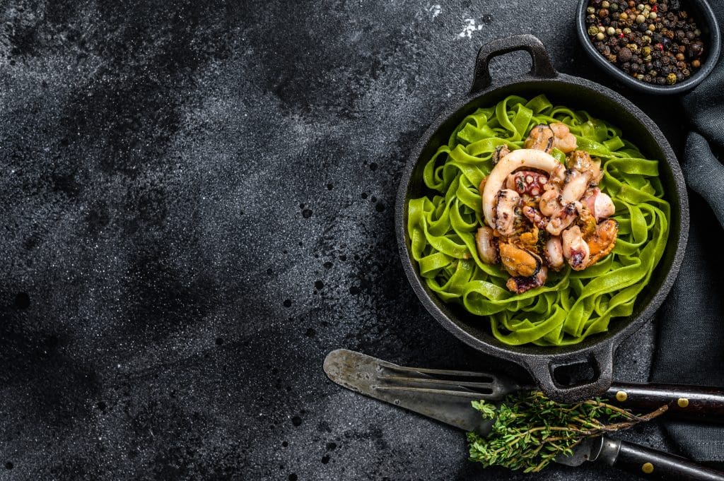 Fettuccine spinach pasta with seafood in cream sauce. Black background. Top view. Copy space