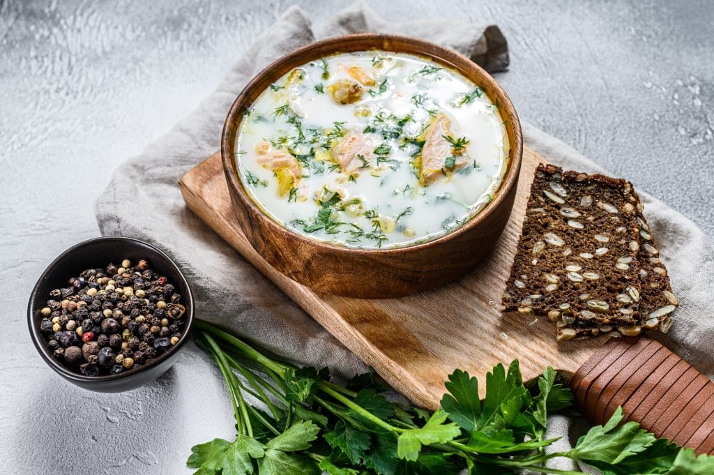 Creamy fish soup with salmon, trout, potatoes and parsley. Gray background, top view.