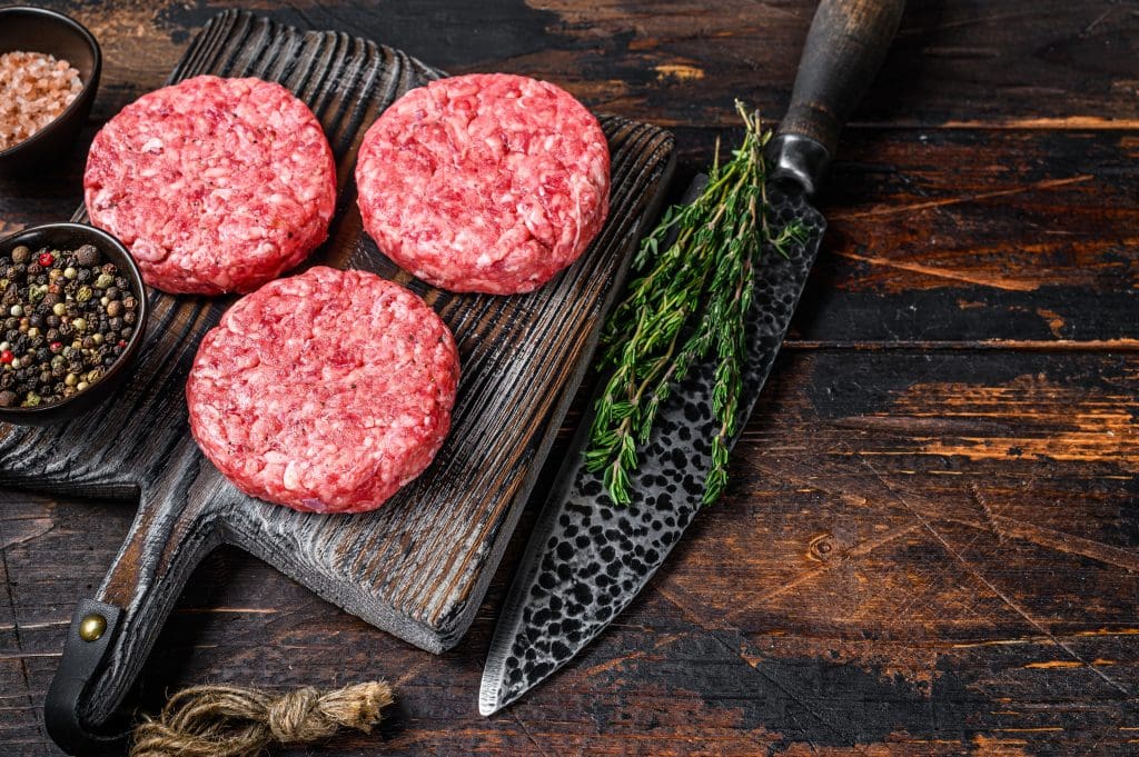 Raw steak burgers patties with ground beef and thyme on a wooden cutting board.
