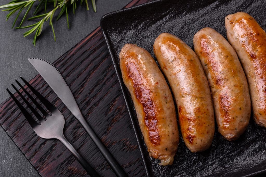 Tasty grilled sausages with spices and herbs on a black slate plate