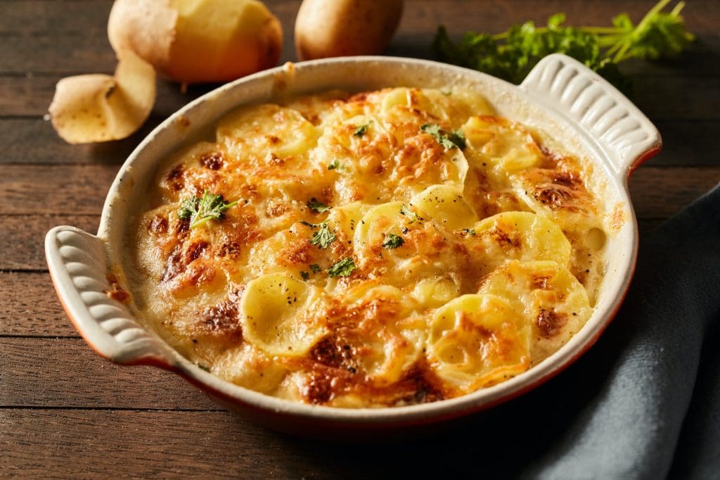 Appetizing baked potatoes with crunchy cheese in ceramic dish