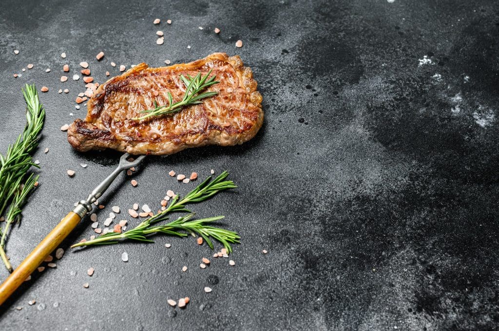 BBQ Strip New York steak or striploin. Black background. Top view. Copy space