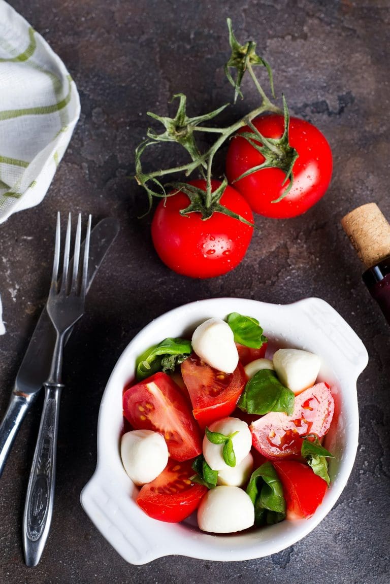 Caprese salad with mozzarella, tomato, basil and balsamic vinegar arranged on white bowl