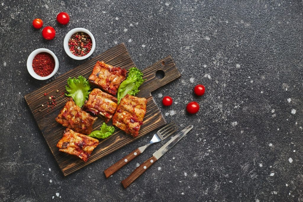 Grilled baked pork ribs with spices and vegetables on wooden cutting board