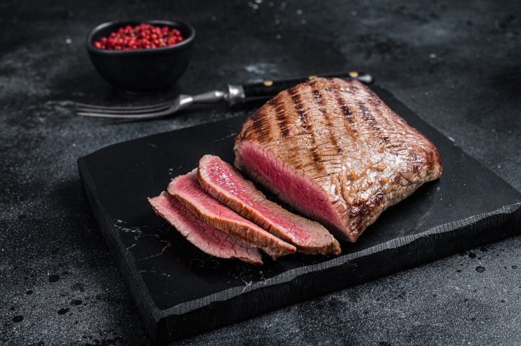 Grilled Flank Steak BBQ on a marble board. Black background. Top view