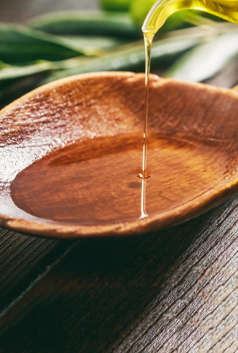Olive oil in a wooden bowl on a table, closeup view