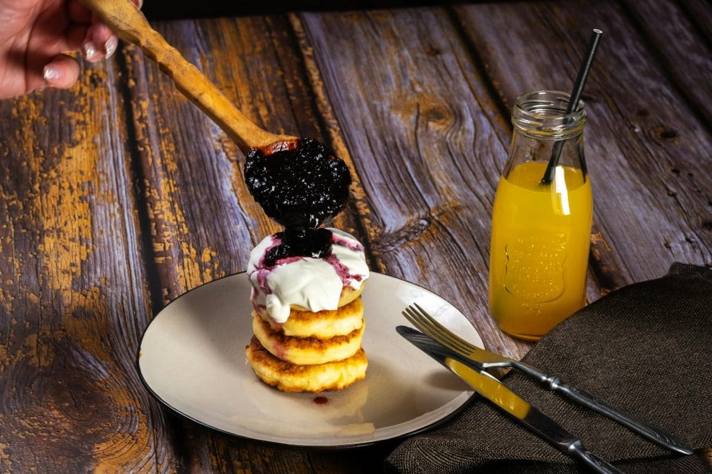 Cheesecakes with blueberry jam and sour cream on a plate with orange juice in a bottle