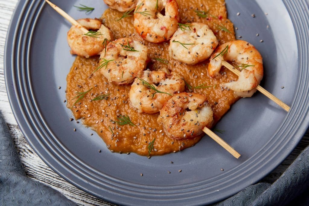 Close up of seafood snacks. Grilled prawns on skewers on the plate.