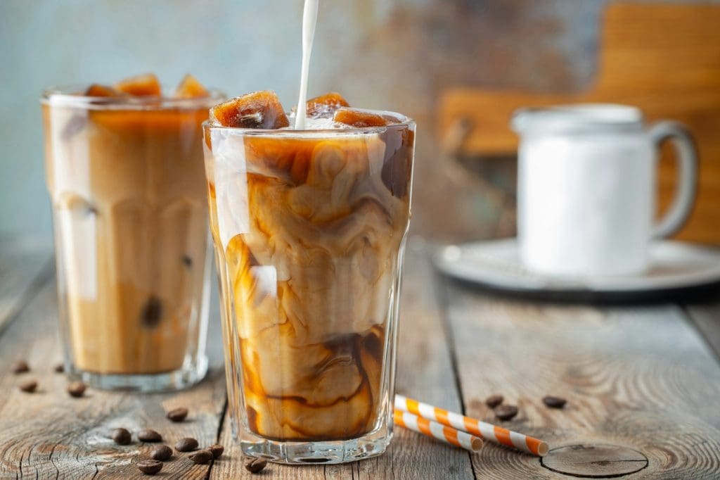 Ice coffee in a tall glass with cream poured over, coffee ice cubes and beans.