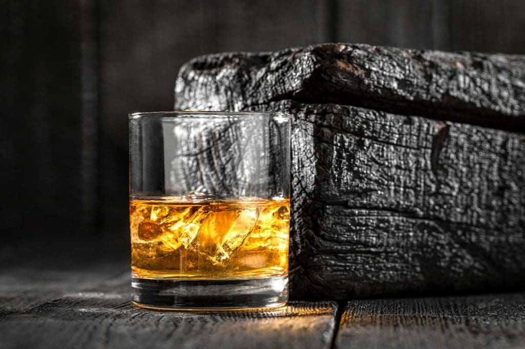 Ice with golden whisky in glass on a burnt wood