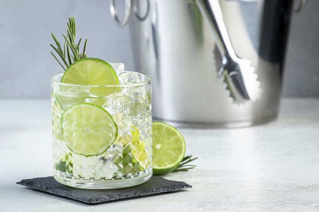 Gin tonic classic cocktail drink with dry gin, bitter tonic, lime and ice. Gray table background
