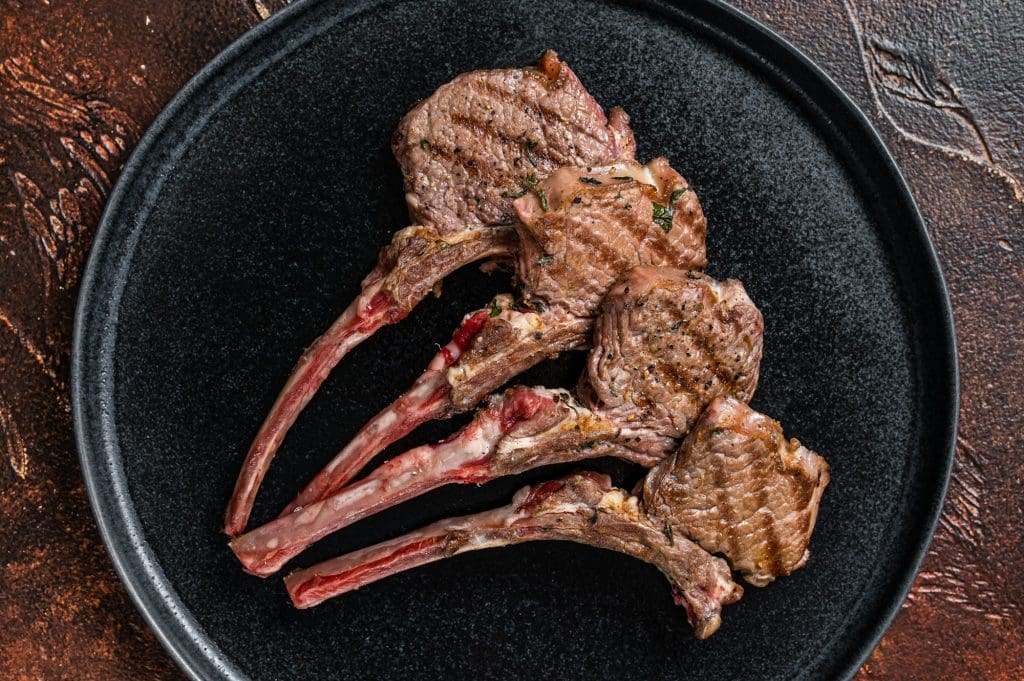 BBQ Grilled lamb chops steaks in a plate. Dark background. Top view