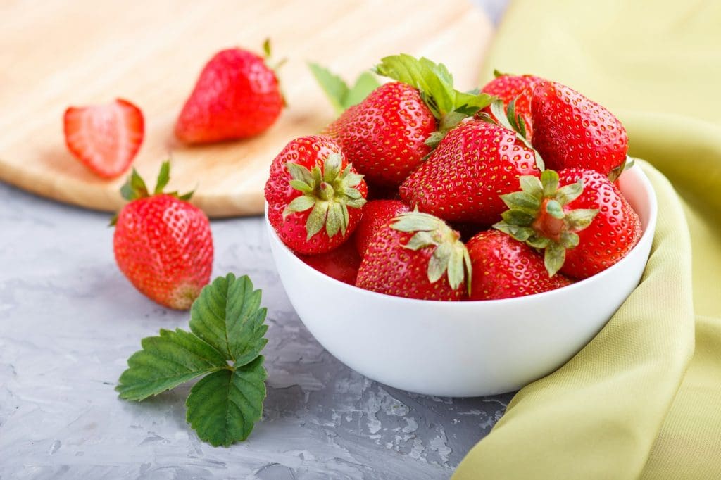 Fresh red strawberry in white bowl on gray concrete background. side view.