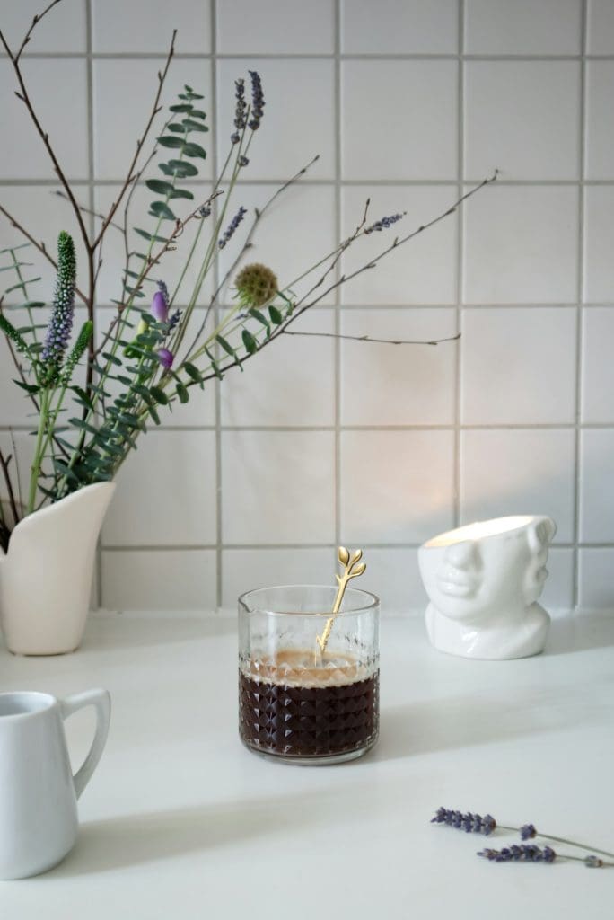 Glass texture cup with black coffee beside vase with bouquet on table in kitchen
