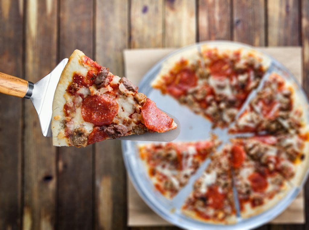 picking up slice of meaty sausage and pepperoni pizza top down view
