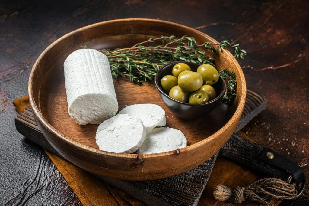 Soft Goat cheese chevre in a plate with thyme and olives. Dark background. Top view. Copy space.