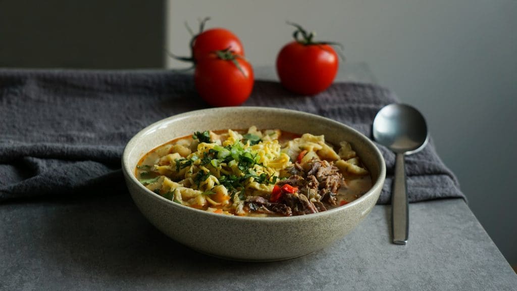 Soup of meat and pasta near tomatoes and spoon