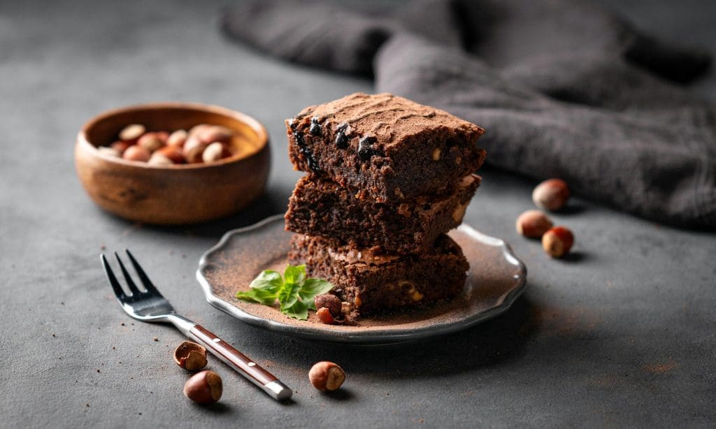 A stack of chocolate brownies with mint and hazelnuts on a dark background with nuts.
