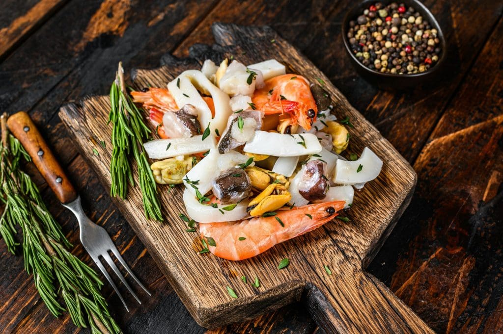 Raw mix seafood cocktail with shrimps, prawns, mussels, squids and octopus on a cutting board.