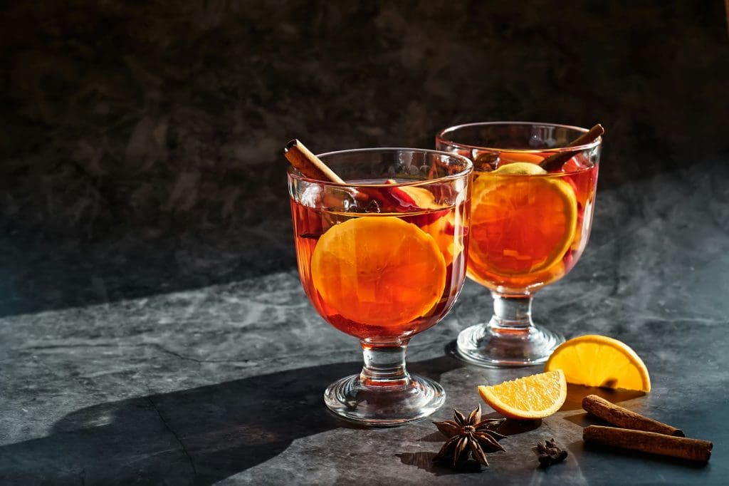 Wine glasses of hot mulled wine with spiced, apple and orange on dark background.