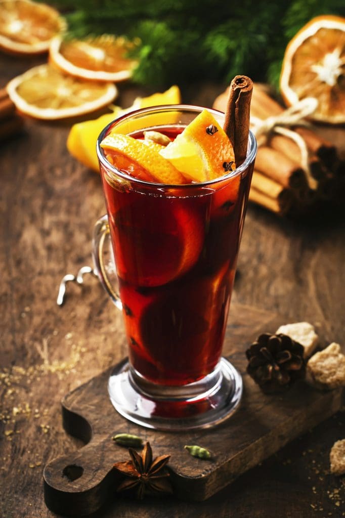 Christmas mulled red wine with spices and fruits in tall glass on wooden rustic table