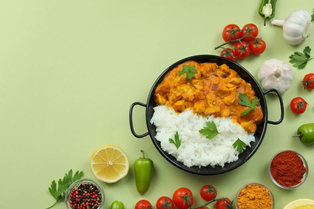 Chicken tikka with ingredients on green background